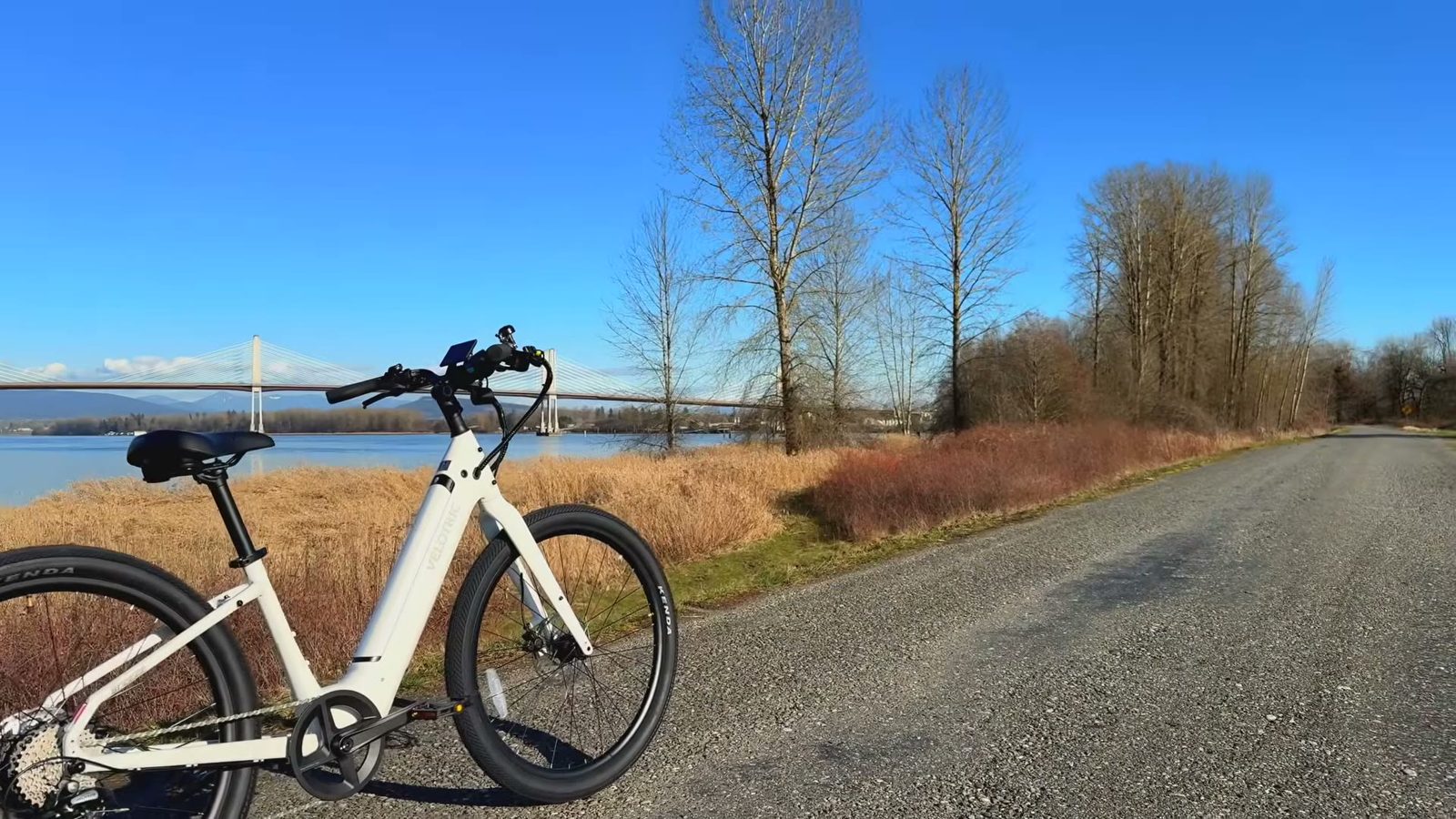 Velotric Breeze 1 parked on a riverside gravel road with a cable-stayed bridge behind it